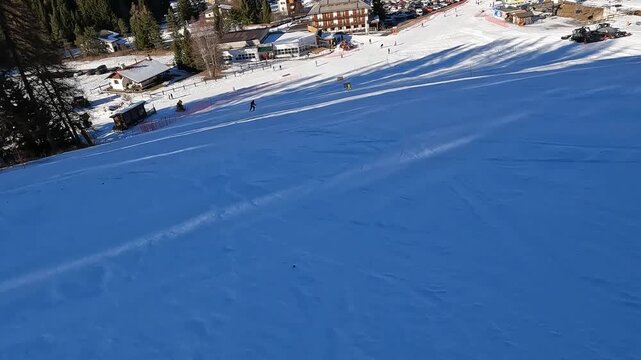 Following a skier carving on wide groomed slope in Folgaria ski resort, Italian Alps winter sports action. Skier carving on white slope during sunny winter day in Folgaria, Italian Alps ski resort wit