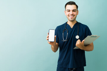 Smiling male doctor or nurse holding smartphone with blank screen and medical clipboard for telemedicine app