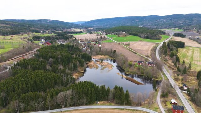 patchwork fields dense evergreen forests surround reflective pond panorama curving roads weave through rolling valleys norway aerials forest drone 