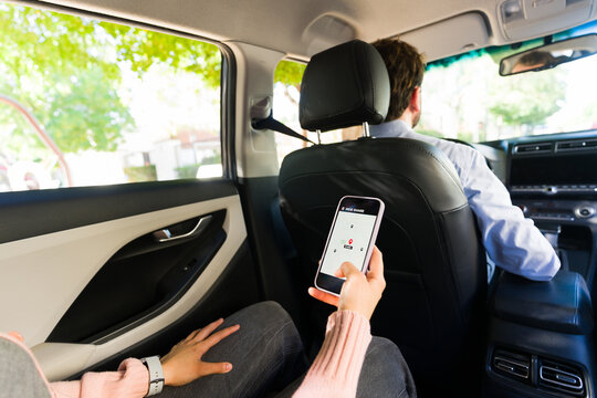 Passenger using rideshare mobile app in car, checking real-time map during urban commute with driver