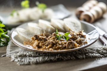 Traditional Szeged goulash with pieces of meat and sauerkraut is served on a plate, complemented by a few slices of light steamed dumplings and garnished with parsley