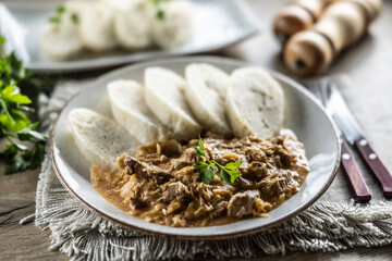 Traditional Szeged goulash with pieces of meat and sauerkraut is served on a plate, complemented by a few slices of light steamed dumplings and garnished with parsley