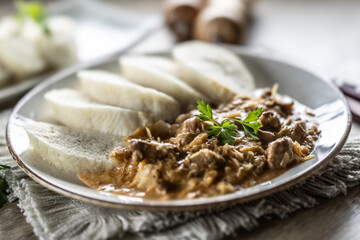 Traditional Szeged goulash with pieces of meat and sauerkraut is served on a plate, complemented by a few slices of light steamed dumplings and garnished with parsley