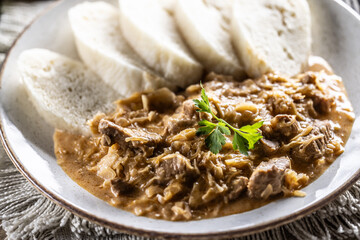 Traditional Szeged goulash with pieces of meat and sauerkraut is served on a plate, complemented by a few slices of light steamed dumplings and garnished with parsley