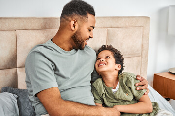 Fototapeta premium Dad and son are sitting on the bed, hugging. A cozy morning at home and spending time together. Fatherhood and family.
