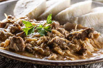 Traditional Szeged goulash with pieces of meat and sauerkraut is served on a plate, complemented by a few slices of light steamed dumplings and garnished with parsley