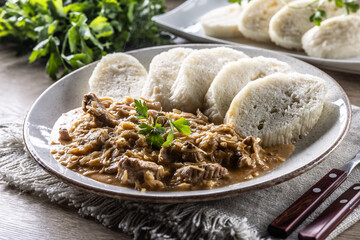 Traditional Szeged goulash with pieces of meat and sauerkraut is served on a plate, complemented by a few slices of light steamed dumplings and garnished with parsley