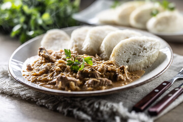 Traditional Szeged goulash with pieces of meat and sauerkraut is served on a plate, complemented by a few slices of light steamed dumplings and garnished with parsley