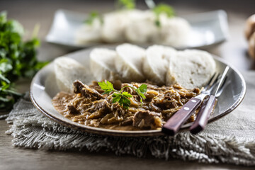 Traditional Szeged goulash with pieces of meat and sauerkraut is served on a plate, complemented by a few slices of light steamed dumplings and garnished with parsley