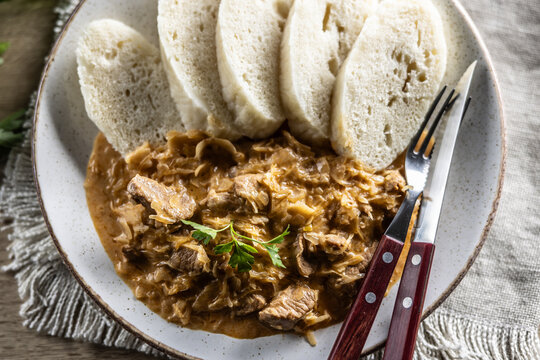 Traditional Szeged goulash with pieces of meat and sauerkraut is served on a plate, complemented by a few slices of light steamed dumplings and garnished with parsley
