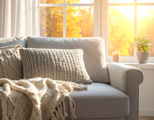 Cozy living room interior with chunky knit blanket on a fabric sofa in warm morning light