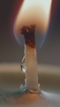 Extreme close-up view of candle wick being lit with matchstick, then burning with wax melting and flame glowing warmly. Vertical clip