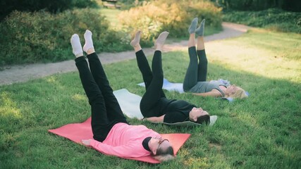 Three middle-aged girlfriends doing fitness exercises in the park. A group of women are doing an exercise lying on mats.