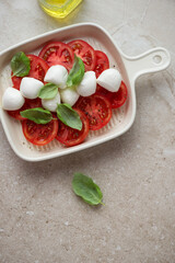 Italian caprese salad with bocconcini in a serving tray, vertical shot on a beige stone background with space, above view