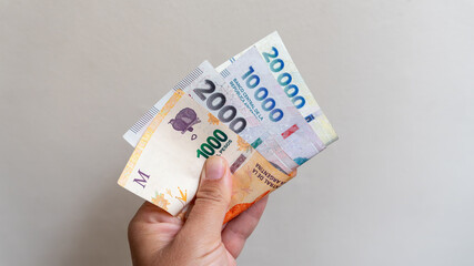 Hand holding argentine peso banknotes, showing different denominations, representing economic inflation