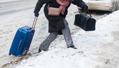 A young woman with a suitcase and bags crosses a snowy road. Winter in the city. Selective focus