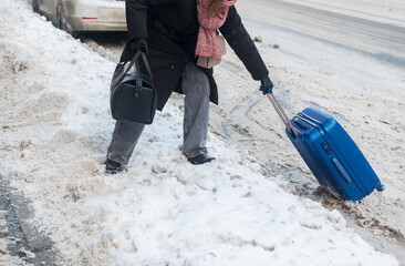 A young woman with a suitcase and bags crosses a snowy road. Winter in the city. Selective focus