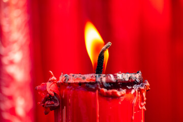 Close up of a burning red candle with melting wax and flame, symbolizing love, passion, spirituality, ritual, meditation, romance, celebration and emotional atmosphere on blurred red backgrounds.