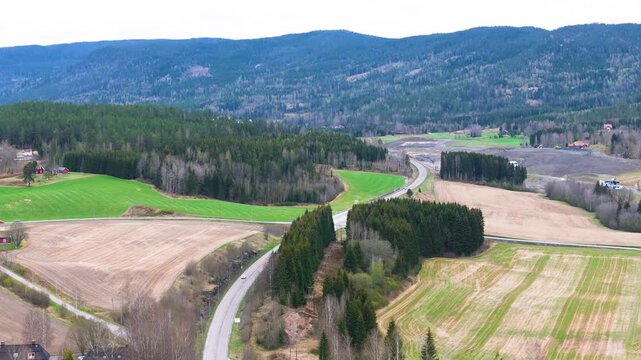 curving country road threads between green meadows plowed fields rolling forested mountains define norway aerials forest smooth drone shot 