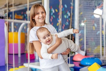 Smiling girl holding baby brother in playroom. Family time