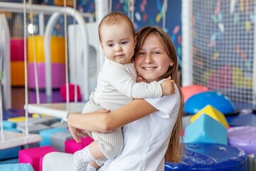 Obraz premium Sister hugging baby in colorful indoor playground. Family time
