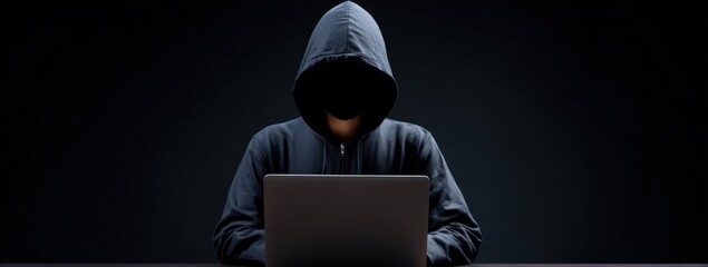 Hooded figure using laptop in dark studio setting