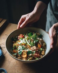 Hands holding a bowl of vibrant quinoa salad with roasted tomatoes, fresh herbs, and creamy dressing, showcasing healthy eating and culinary creativity in a rustic kitchen setting