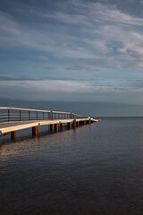 Obraz premium A quiet wooden pier stretching into calm sea water under a dramatic cloudy sky, creating a peaceful and minimal coastal scene.