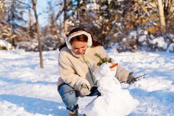 Young adult woman making snowman outdoors in winter
