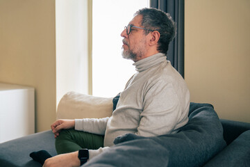 Fototapeta premium Senior man sitting quietly on sofa at home in calm reflective moment