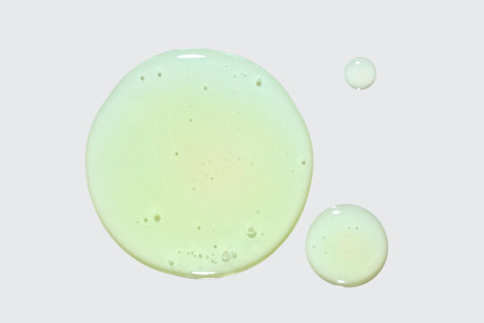 Liquid green gel cosmetic smudge drops texture on light grey white isolated background. Beauty product sample swatch