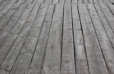 Old wooden walkway made of gray cracked boards with rusty nails and visible gaps, creating an abandoned atmosphere.