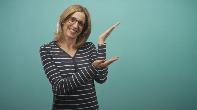 Woman wearing striped top and glasses presenting with palms up and smiling in studio; welcoming approachability.