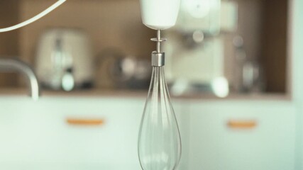 A domestic kitchen scene unfolds as a blender attachment is firmly secured, poised to whip eggs and cream into a smooth mixture, filling the warm atmosphere with culinary preparation