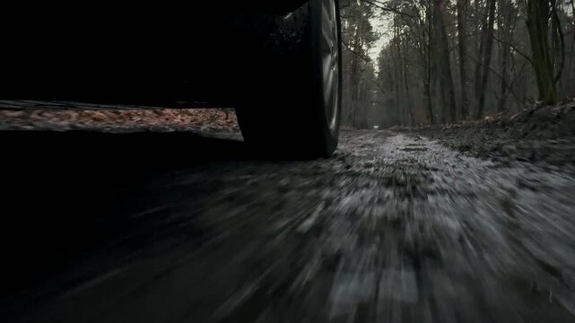 As vehicle navigates forest terrain, its rear tire spins vigorously, spewing liquid mud splashing through puddles rugged automotive transportation route, demonstrating challenges driving unpaved roads