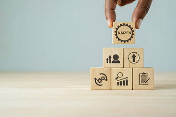 Kaizen Concept: A hand delicately balances a wooden block bearing the word Kaizen atop a stack of blocks representing continuous improvement.