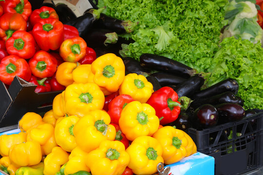 crates of fruit for sale at the produce stall featuring red and yellow peppers ripe eggplant and green lettuce