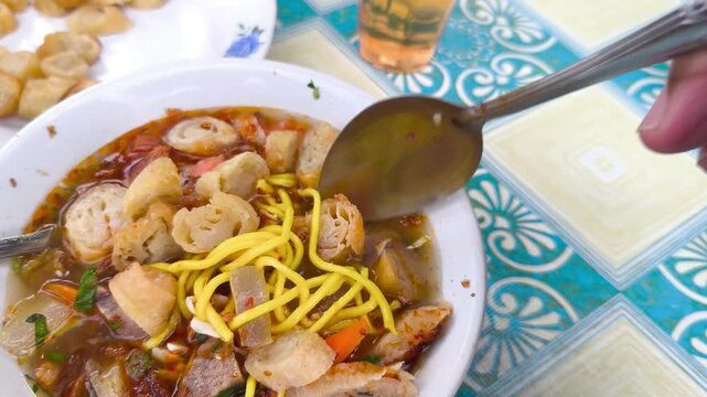 A bowl of soto mie, a traditional Indonesian dish from Bogor, with a spoon scooping up noodles and vegetables on a colorful table.