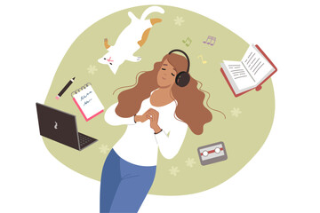 Woman listens to music on headphones, lies on lawn near cat and textbooks and takes break from work. Young girl student or freelancer enjoying relaxing music or educational audio book