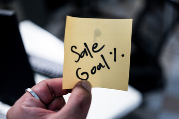 Man holding a yellow sticky notes with the word Sale Goal % for collaborative planning and strategy development for business initiatives and projects.