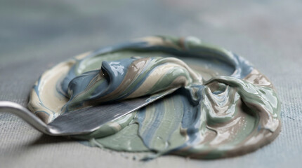 photorealistic macro of thick textured acrylic paint in muted blue grey and beige tones being mixed with a metal palette knife on a canvas for fine art and creative hobby concept