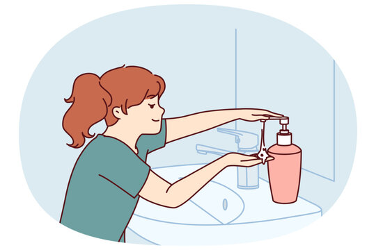 Little girl uses liquid soap to wash hands standing near sink and mirror in bathroom. Child follows hygiene rules with smile and washes hands with soap after coming home from school.