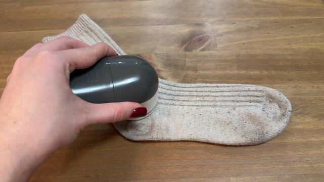 Cleaning sock with fabric shaver. Hand removing lint from sock. Sock care with electric lint remover. Knit sock cleaning close up.