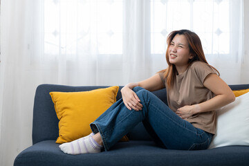 Woman with abdominal pain: A woman is depicted sitting on a sofa, visibly experiencing discomfort and holding her abdomen, suggesting abdominal pain or a stomachache.