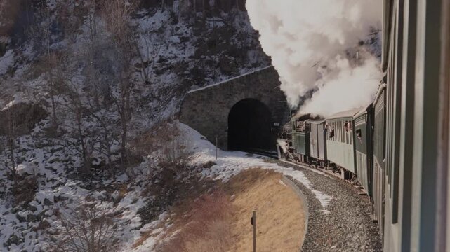 A steam locomotive driving through the Swiss alps in the winter.