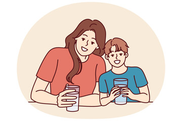 Happy mom and son drink water from transparent glasses and smile enjoying clean refreshing beverage. Positive family with water look at camera together and smile urging to drink more liquid