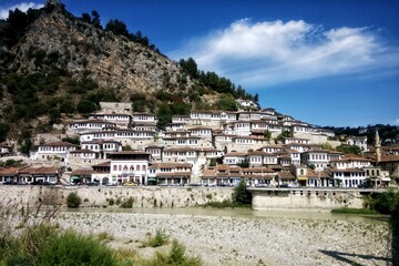 Obraz premium A hillside view of the historic district of the UNESCO city of Berat, Albania, known for its traditional Ottoman-era houses with many windows and a rocky riverbed in the foreground