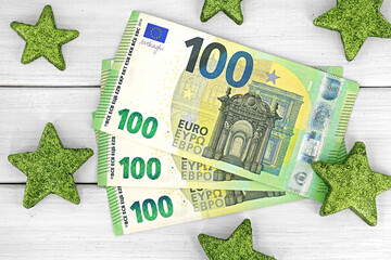 top view of three one hundred euro banknotes on white wooden background with glittering green stars, Banknotes of 100 euros on table, concept of extra salary or cash winnings