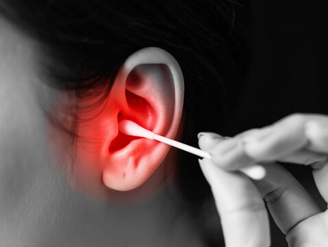 Earache pain Close up of ear with red inflammation being cleaned by cotton swab cleaning