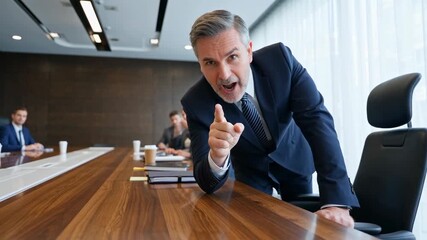 European middle-aged businessman pointing finger angrily during intense boardroom confrontation with colleagues in modern corporate office